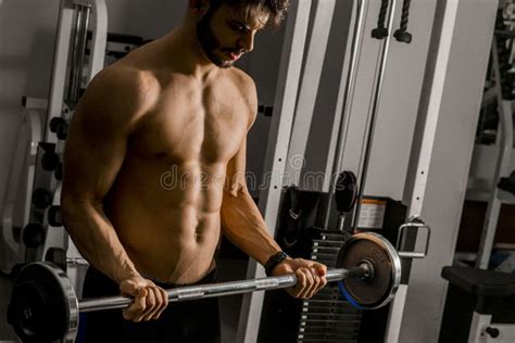 Portrait Of Young Man Flexing Muscles With Barbell In Gym Stock Photo
