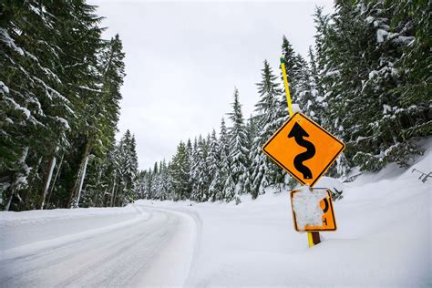 Low Angle View Of A Winding Road Sign Alongside A Snow Covered Mountain