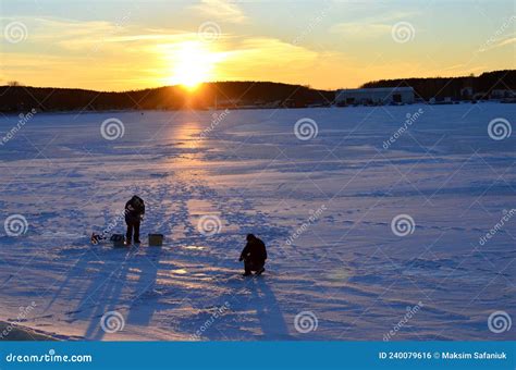 Two Fishermen On A Frozen Lake Catch Fish In A Hole Of Ice On The