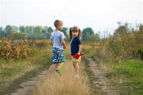 Little Boy And Little Girl Playing Outside On Field Gravel Road On A
