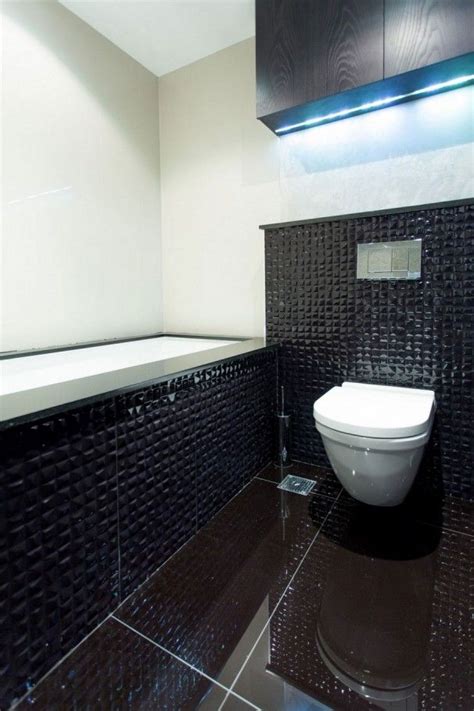 A White Toilet Sitting In A Bathroom Next To A Black Tiled Wall And