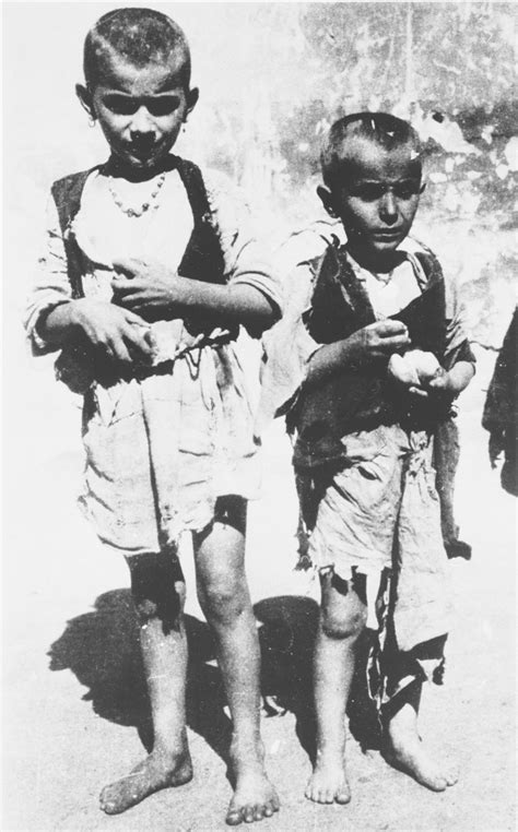 Two Barefoot Emaciated Children Pose Outside Holding A Bit Of Food At