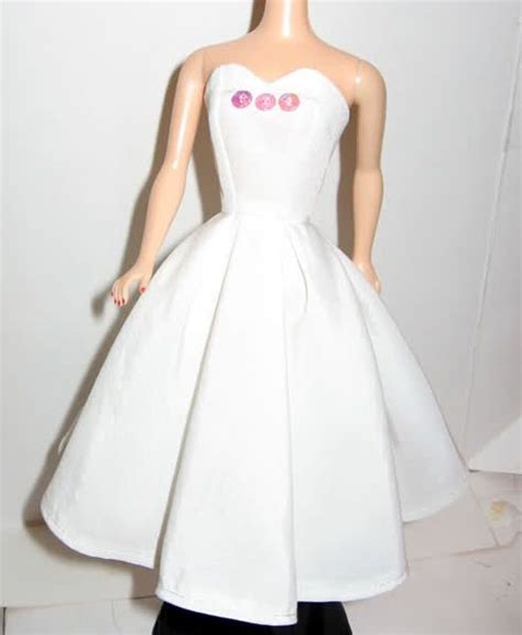 The Doll Is Wearing A White Dress With Pink Buttons