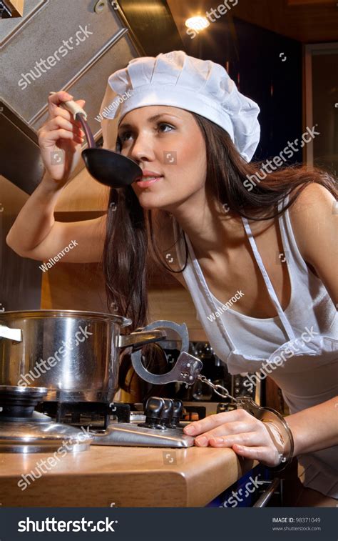 Portrait Of Sexy Housewife Chained By Handcuffs To A Pan She Tasting Dish In Kitchen Room Stock