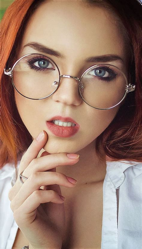 A Woman With Red Hair And Glasses Is Posing For The Camera While Holding Her Hand To Her Chin