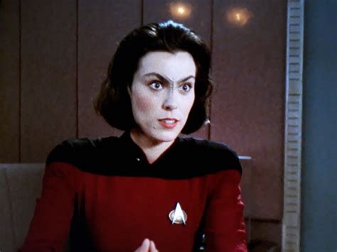 A Woman In A Star Trek Uniform Sitting At A Table With Her Hand On Her