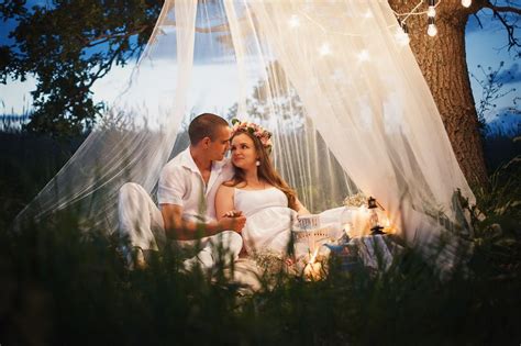 Жених и невеста сидят в белом шалаше на зеленой траве между деревьев