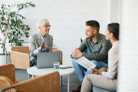 Happy Mature Insurance Agent Using Laptop While Communicating With Young Couple On A Meeting In