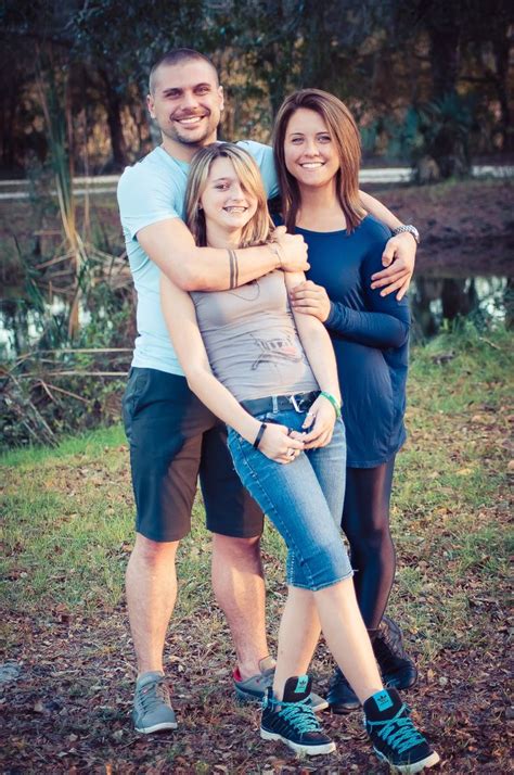 A Man And Two Women Hugging Each Other In Front Of A Pond With Trees