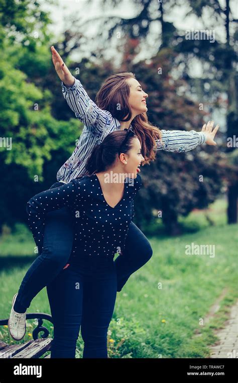 Outdoor Shot Of Young Woman Carrying Her Female Friend On Her Back Two