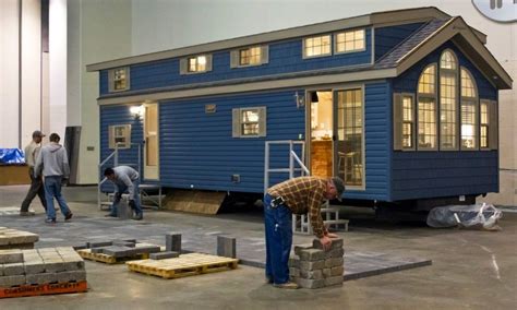 Two Men Working On A Tiny Blue House In A Building That Is Being Built