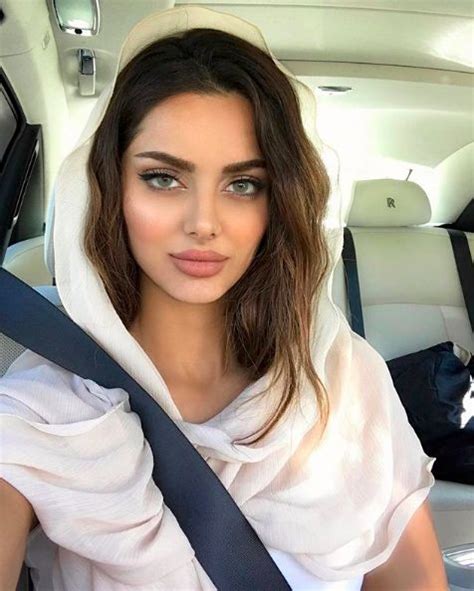 A Woman Sitting In The Back Seat Of A Car Wearing A White Shirt And Scarf