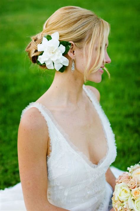 a woman sitting in the grass with flowers in her hair and wearing a wedding dress