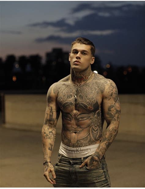 A Man With Tattoos On His Chest Standing In Front Of A Cityscape At Night