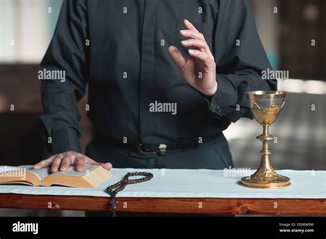 Close Up Of Priest Standing At The Altar With Bible And Rosary Beads