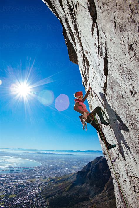 Female Rock Climber On A Sheer Cliff On A Mountain Overlooking A City
