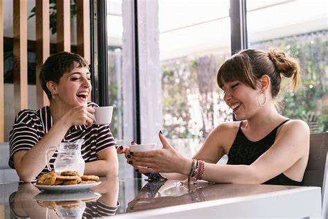 Cute Girlfriends Laughing While Having A Coffee At Home By Luis