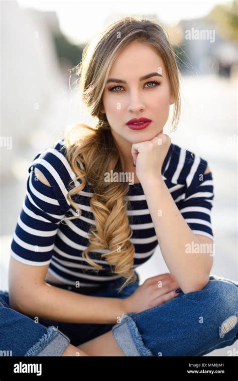 Blonde Woman Model Of Fashion Sitting On A Bench In Urban Background