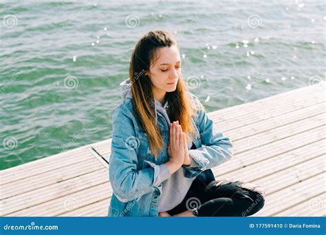 A Young Beautiful Girl Is Sitting On A Pier Near The Lake And Doing