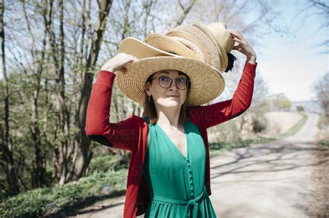 Portrait Of Mature Woman With Stack Of Straw Hats On Her Head Outdoors