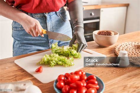 Woman With Prosthesis Arm Is Cutting Salad On Table Stock Photo