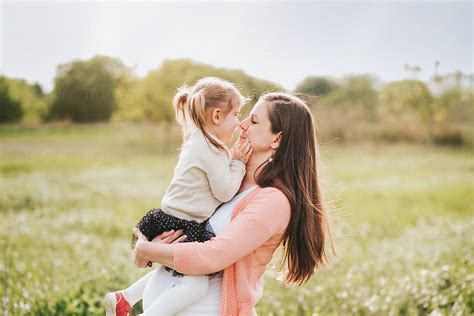 pregnant mother playing with her daughter outdoors in a field hugging and kissing her by