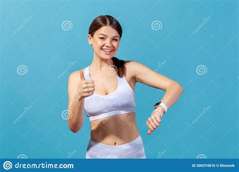 Happy Athletic Woman In White Sportswear Showing Thumbs Up Demonstrating Smartwatch On Her Wrist