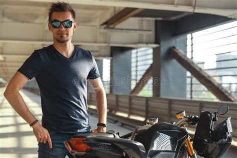 Portrait Of Attractive Biker Standing Next To Motorcycle At Parking