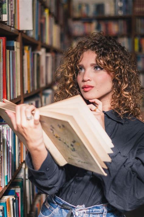 A Woman Is Holding An Open Book In Front Of A Bookshelf Full Of Books