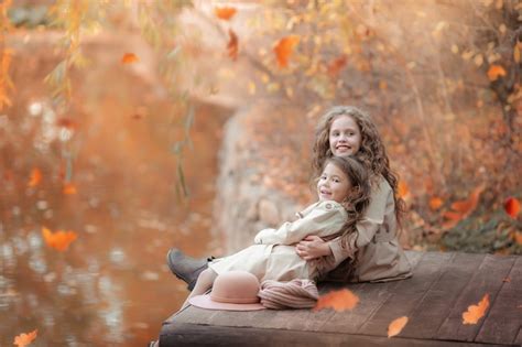 Premium Photo Two Sisters Sit On A Wooden Pier In The Autumn On The