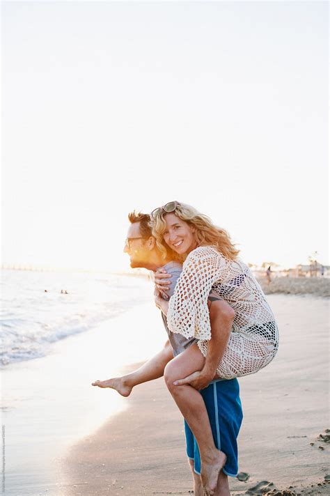 Husband Giving His Wife A Piggyback Ride On Beach Del Colaborador De