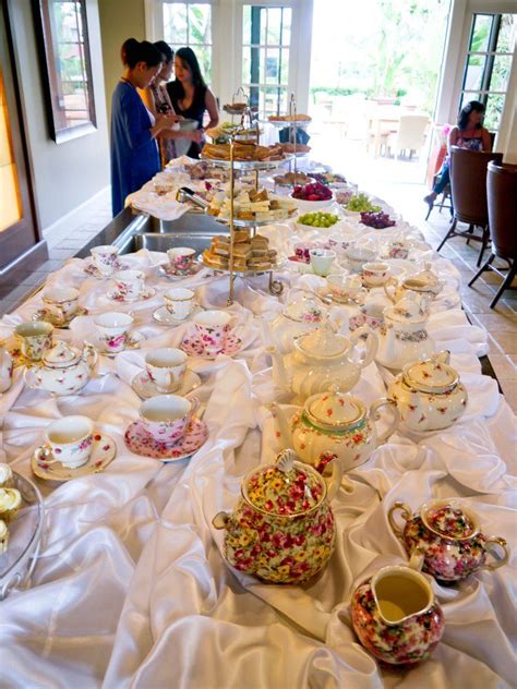 A Long Table Covered In Tea Cups And Saucers With People Sitting At The