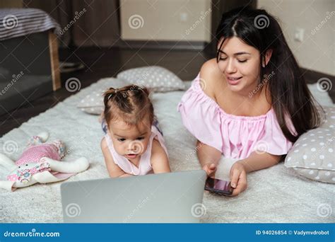 Smiling Mother Chatting By Phone While Her Daughter Using Laptop Stock