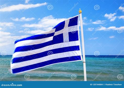 Greek Flag Waving In Wind In Blue Sky And White Clouds And Sea Waves