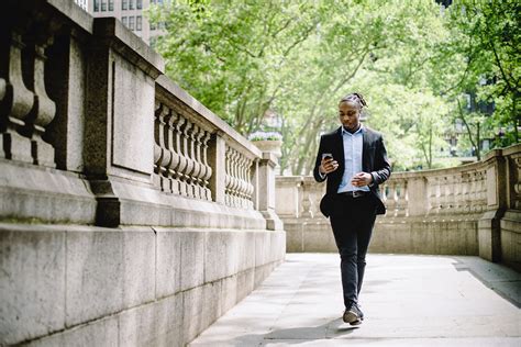 Concentrated Black Businessman Walking In City Park And Messaging On