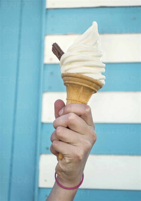 Close Up Of Girls Hand Holding Ice Cream Cone Against Striped Wall