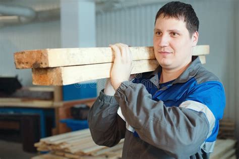 A Sawmill Worker In Overalls Carries Wooden Bars On His Shoulder