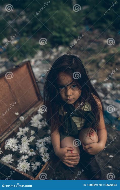 A Homeless Girl Is Sitting On A Garbage Dump Next To A Suitcase With