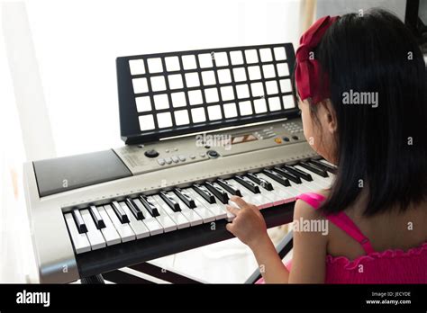 Asian Chinese Little Girl Playing Electric Piano Keyboard In The Living