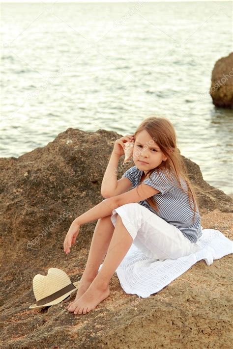 Happy Cute Little Girl With A Beautiful Smile Is Sitting On The Beach