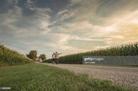 Caucasian Father And Son Walking On Dirt Path By Corn Field High Res