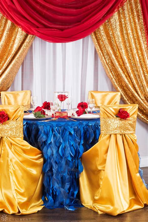 The Table Is Decorated With Red Roses And Blue Ruffles Along With Gold