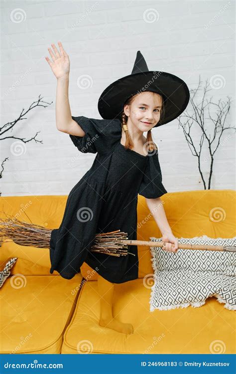 Playful Little Girl Dressed As A Witch Sitting On A Broom Waving Her