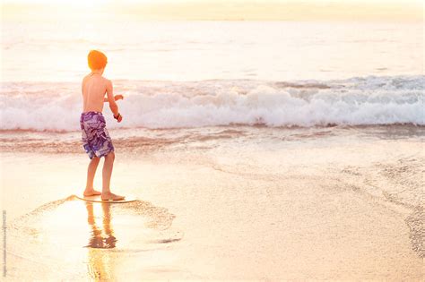 Riding A Skim Board At The Beach At Sunset Del Colaborador De Stocksy