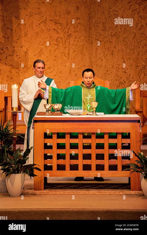 A Robed Deacon And An Asian American Priest Celebrate Mass At The Altar