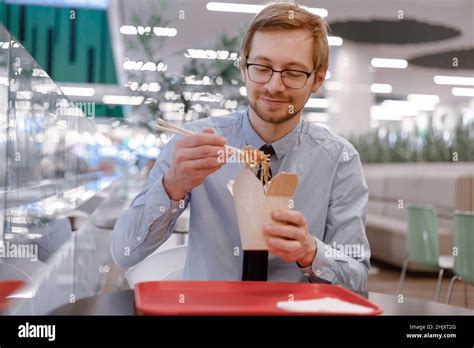 Hungry Man Trader In Shirt Eating Chinese Wok From Box On Food Court