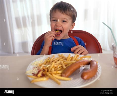 Little Boy Is Eating French Fries And Sausages With Mayonnaise Stock