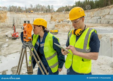 Female Engineer Using Geodetic Station By Her Colleague Stock Photo