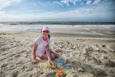 Girl Sitting On Beach Playing In Sand Looking At Camera Smiling Stock Photo Dissolve