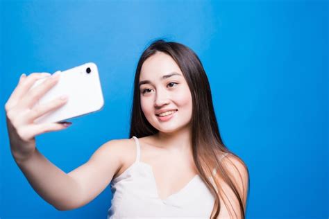 Free Photo Smiling Young Asian Woman Taking A Selfie With Mobile Phone Over Isolated Gray Wall